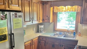 A compact kitchen with wooden cabinets, a built-in refrigerator, a coffee maker, and a window with a view of trees. - Camp Dragonfly Limit 10 3 Bedroom Home by RedAwning (Naples)
