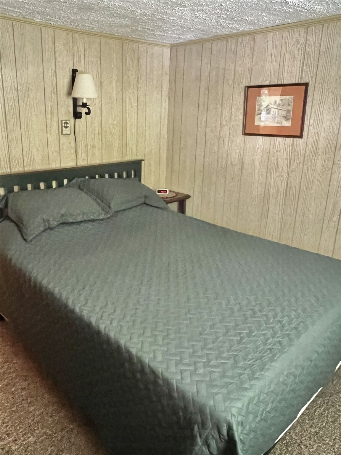 A single bed with a green quilt in a room with wooden panel walls.