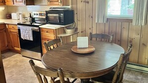 A kitchen with wooden cabinets, a stove, a microwave, and a dining table with chairs. - Camp Dragonfly Limit 10 3 Bedroom Home by RedAwning (Naples)