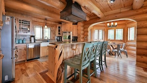 Une cuisine rustique aménagée dans une cabane en rondins, avec des meubles en bois, des appareils en acier inoxydable et un îlot central doté de tabourets de bar.