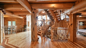 L’intérieur d’une cabane en rondins, avec un escalier en bois, un coin repas et de grandes fenêtres.