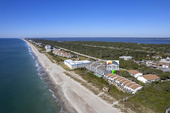 An aerial view of a coastal area with a beach, a large building labeled 'SPECTRUM RENTAL PROPERTIES,' and surrounding residential buildings.