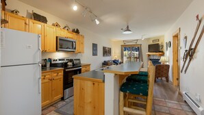A kitchen with wooden cabinets, a refrigerator, a microwave, and a stove. There is a dining area with a table and chairs. - 2656 Tenderfoot Lodge 2 Bedroom Condo by RedAwning (Keystone)