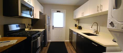 A modern kitchen with stainless steel appliances, wooden flooring, and white cabinetry.