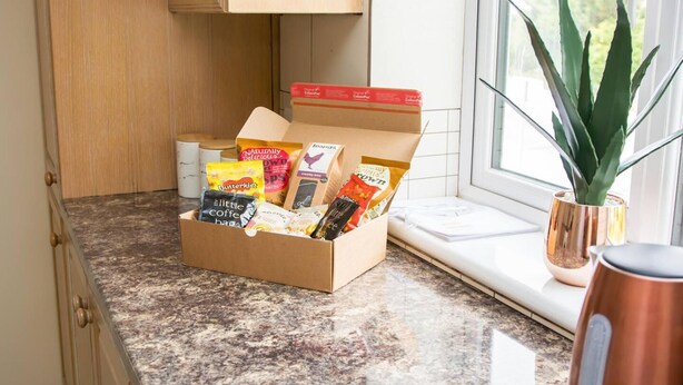 A kitchen with a marble countertop, a box of assorted snacks, a potted plant, and a coffee maker. - Charming 2-bed Apartment in Stroud (Stroud)