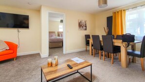A modern living room with a sofa, a coffee table, and a TV. There is a dining area with a table and chairs. - Charming 2-bed Apartment in Stroud (Stroud)