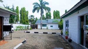 Une cour dallée avec un palmier, un bâtiment blanc doté d’un toit végétalisé et des plantes en pot le long du chemin.