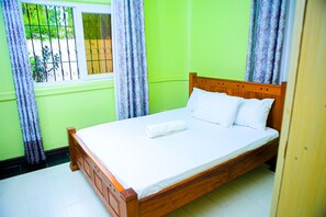 A single-bed room with a wooden headboard, white bedding, and a window with metal bars. - The Nest Resort (Mombasa)
