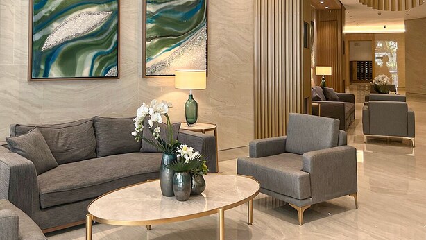 A modern lobby with a curved ceiling, two large abstract paintings, a sofa, armchairs, a coffee table with flowers, and a lamp. - Chic Studio in Lush Residences Near Circuit Makati (Makati)