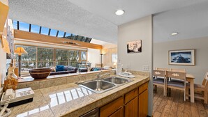 A modern kitchen with granite countertops, stainless steel sinks, and wooden cabinets. There is a dining area with a table and chairs, and a large window offering a view of trees. - Ideal Location in Keystone; 10 min Walk to Lifts/Shops/Lake w/ Scenic Views (Keystone)