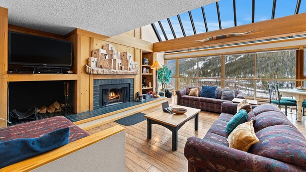 A spacious living room with a fireplace, wooden beams, and large windows offering a view of the outdoors. - Ideal Location in Keystone; 10 min Walk to Lifts/Shops/Lake w/ Scenic Views (Keystone)
