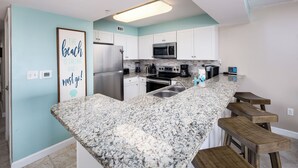 A kitchen with white cabinets, a granite countertop, a stainless steel refrigerator, a microwave, and a coffee maker.