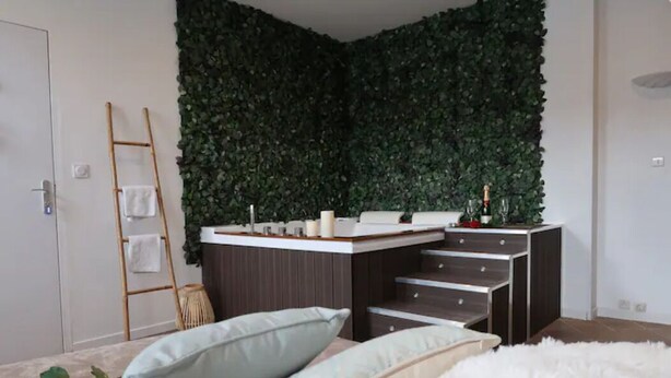A bedroom with a bed, pillows, a white fluffy rug, a wooden ladder, and a wall covered with green foliage.
