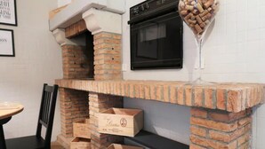 A kitchen with a brick fireplace, a black oven, and wine glasses on the mantel.