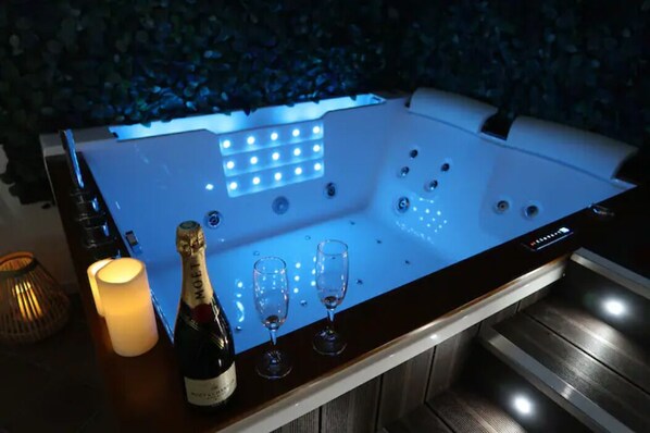 A modern, illuminated hot tub with a bottle of champagne and two glasses on the side. - La Suite - Jacuzzi (Saint-Valery-en-Caux)