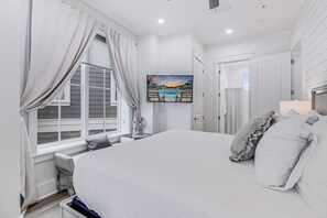 Une chambre avec un grand lit, une fenêtre avec des rideaux, un tableau au mur et une table de chevet avec une lampe.