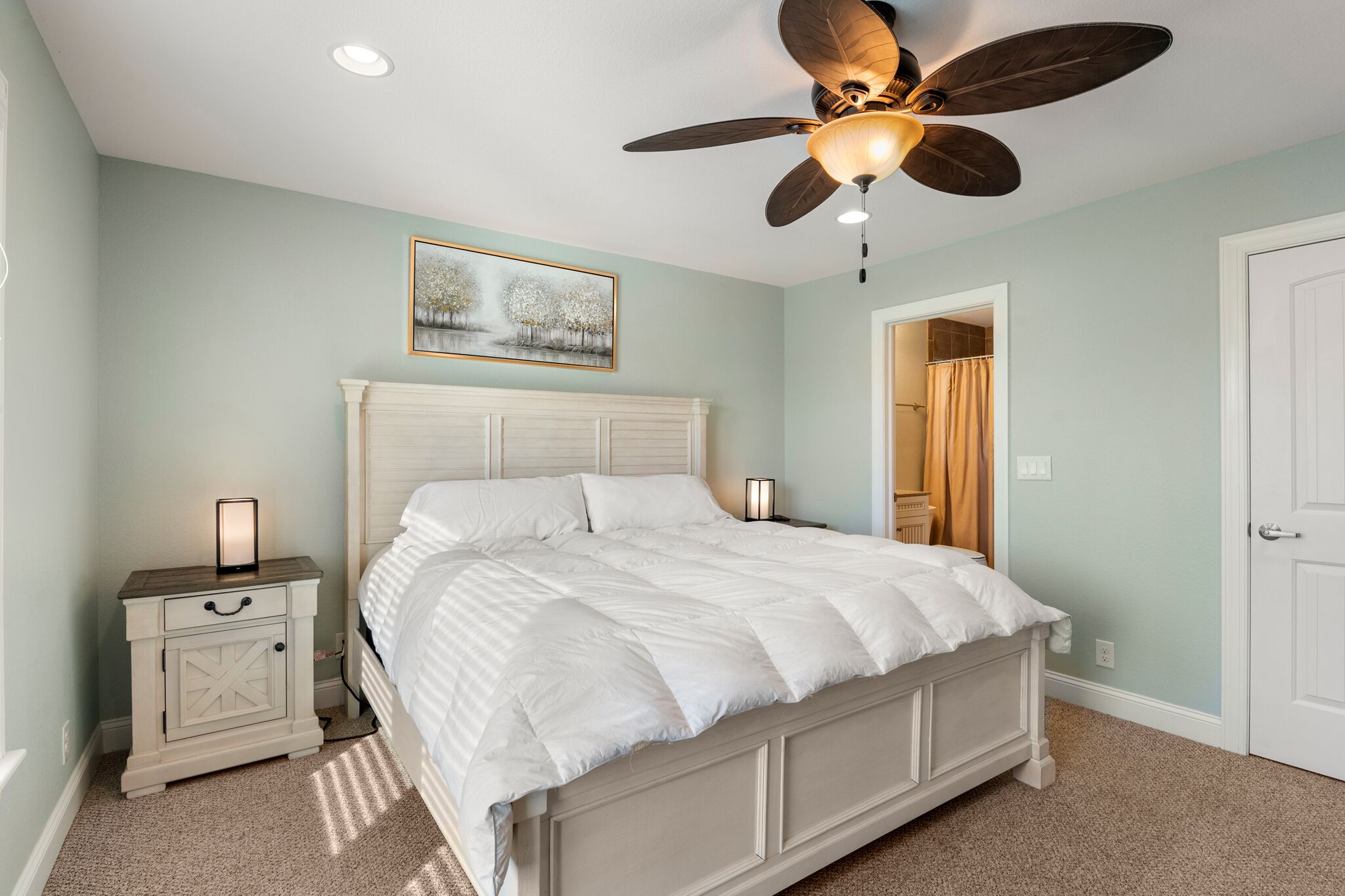 A bedroom with a bed, nightstand, ceiling fan, and a painting on the wall.