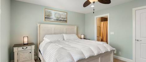 A bedroom with a bed, nightstand, ceiling fan, and a painting on the wall.