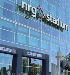 A modern building with a glass facade, a sign reading 'nrg stadium,' and a 'CLUB ENTRANCE' sign below.