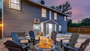 Una casa con una chimenea en el patio trasero, rodeada de sillas Adirondack.