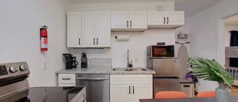 A compact kitchen with white cabinets, a stainless steel refrigerator, a microwave, and a coffee maker.