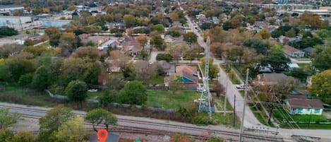 An aerial view of a suburban area with a railway track, residential houses, and a distant city skyline.