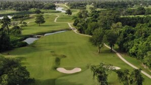 Un campo de golf con un obstáculo acuático, búnkeres de arena y un fairway bien cuidado.