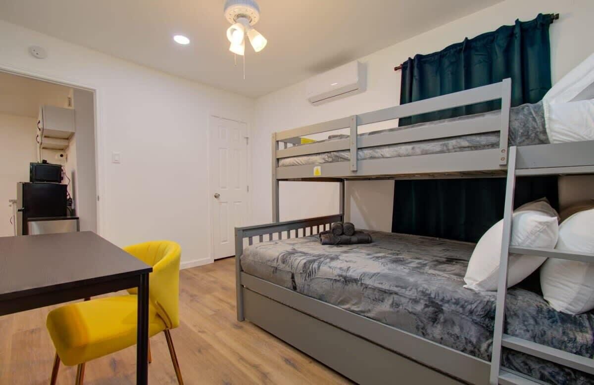 A bunk bed with a grey frame, a table with a dark surface, and a yellow chair.