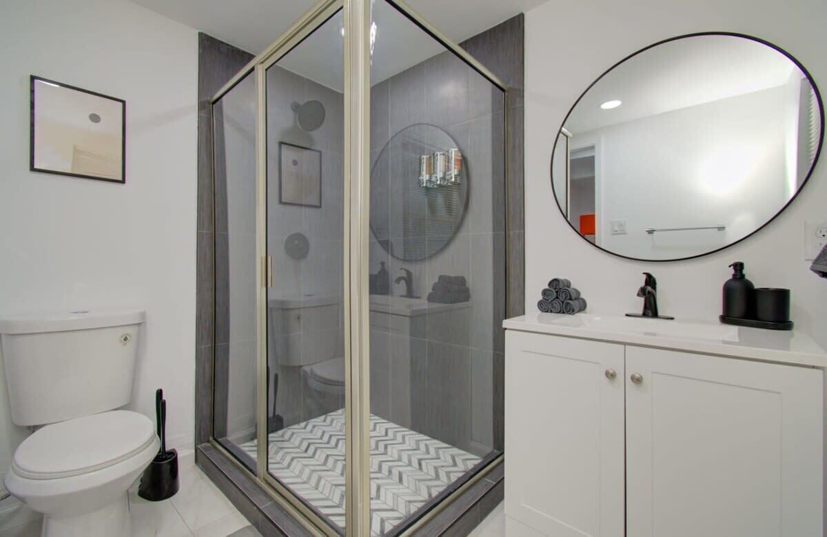 A modern bathroom with a glass-enclosed shower, a toilet, a sink with a mirror, and a toilet paper holder.