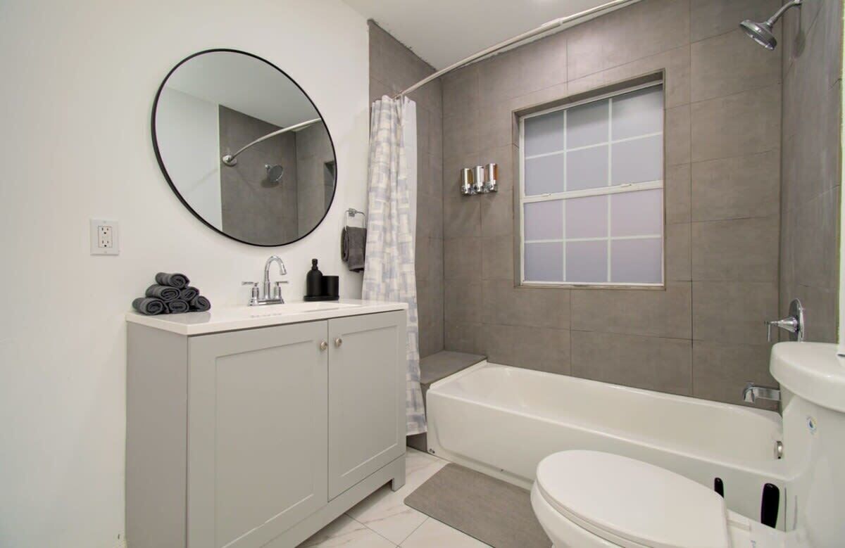 Une salle de bain avec un lavabo blanc, un miroir rond, une baignoire et des toilettes.