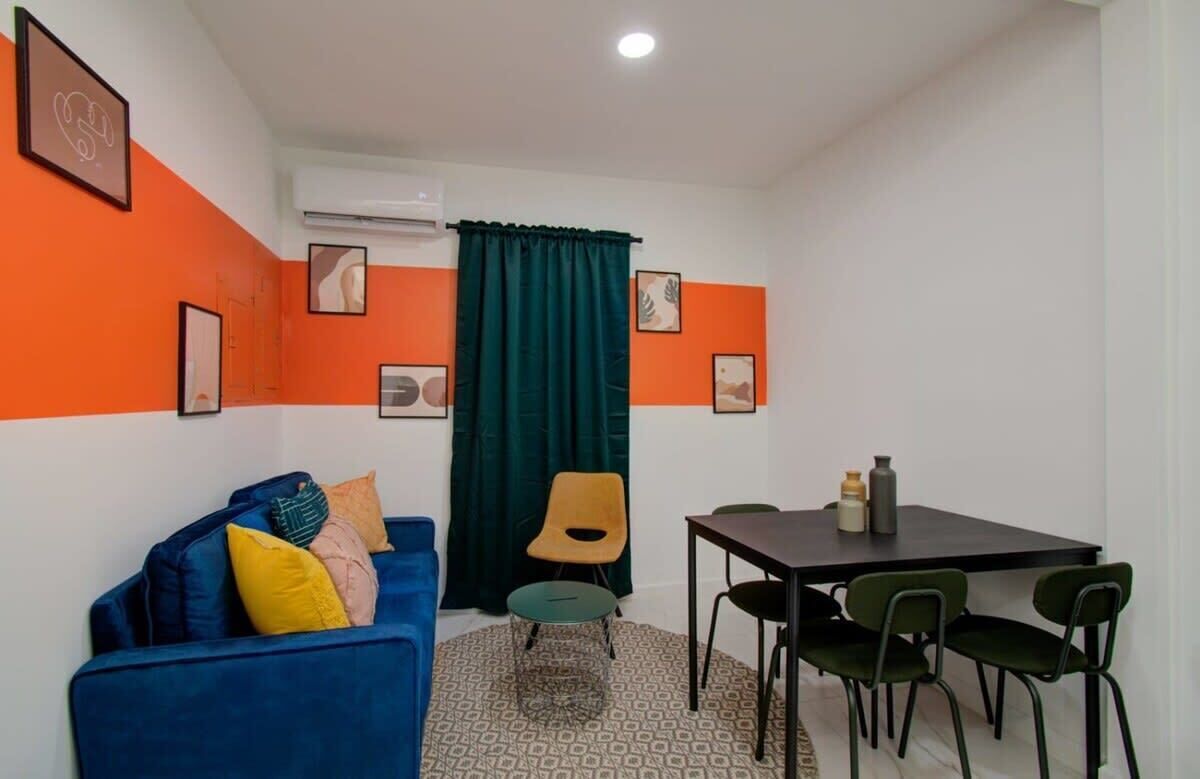A room with a blue sofa, a dining table with chairs, a green chair, and a patterned rug.