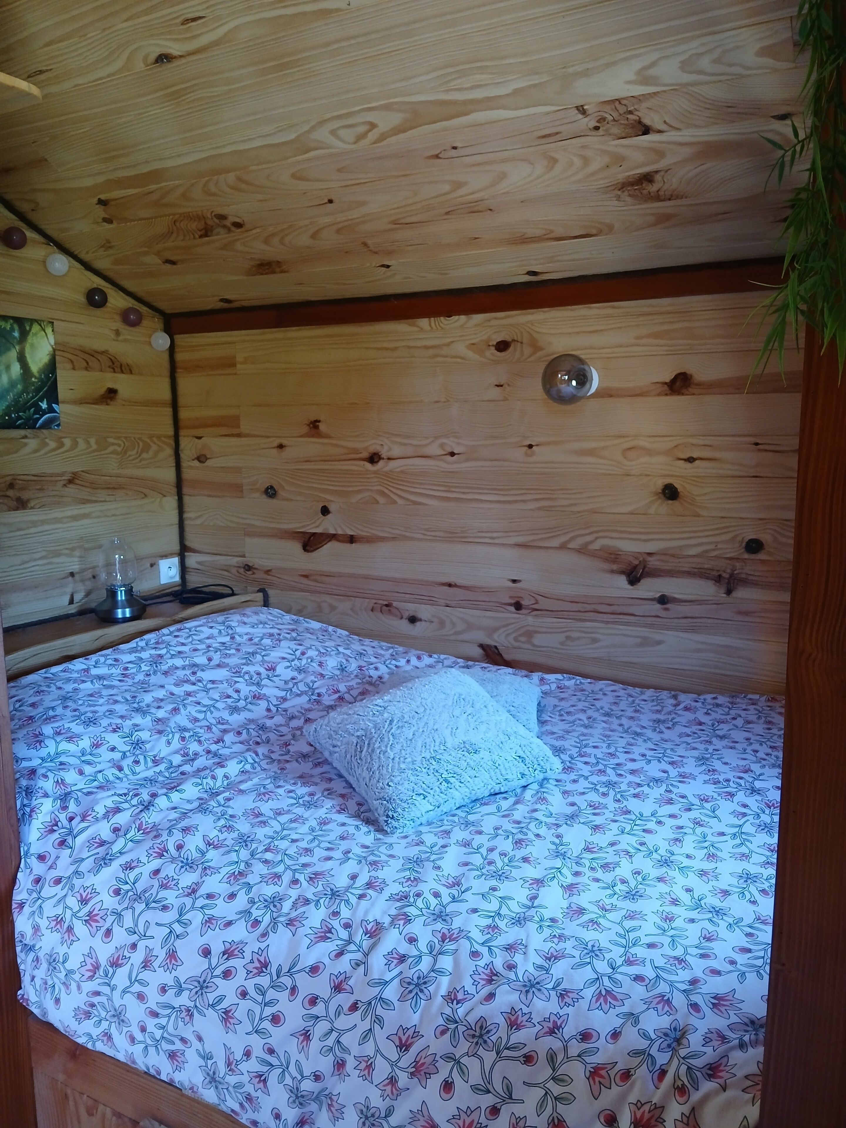 Een slaapkamer in een houten chalet, met een bed, een nachtkastje, een lamp en een wandlamp.
