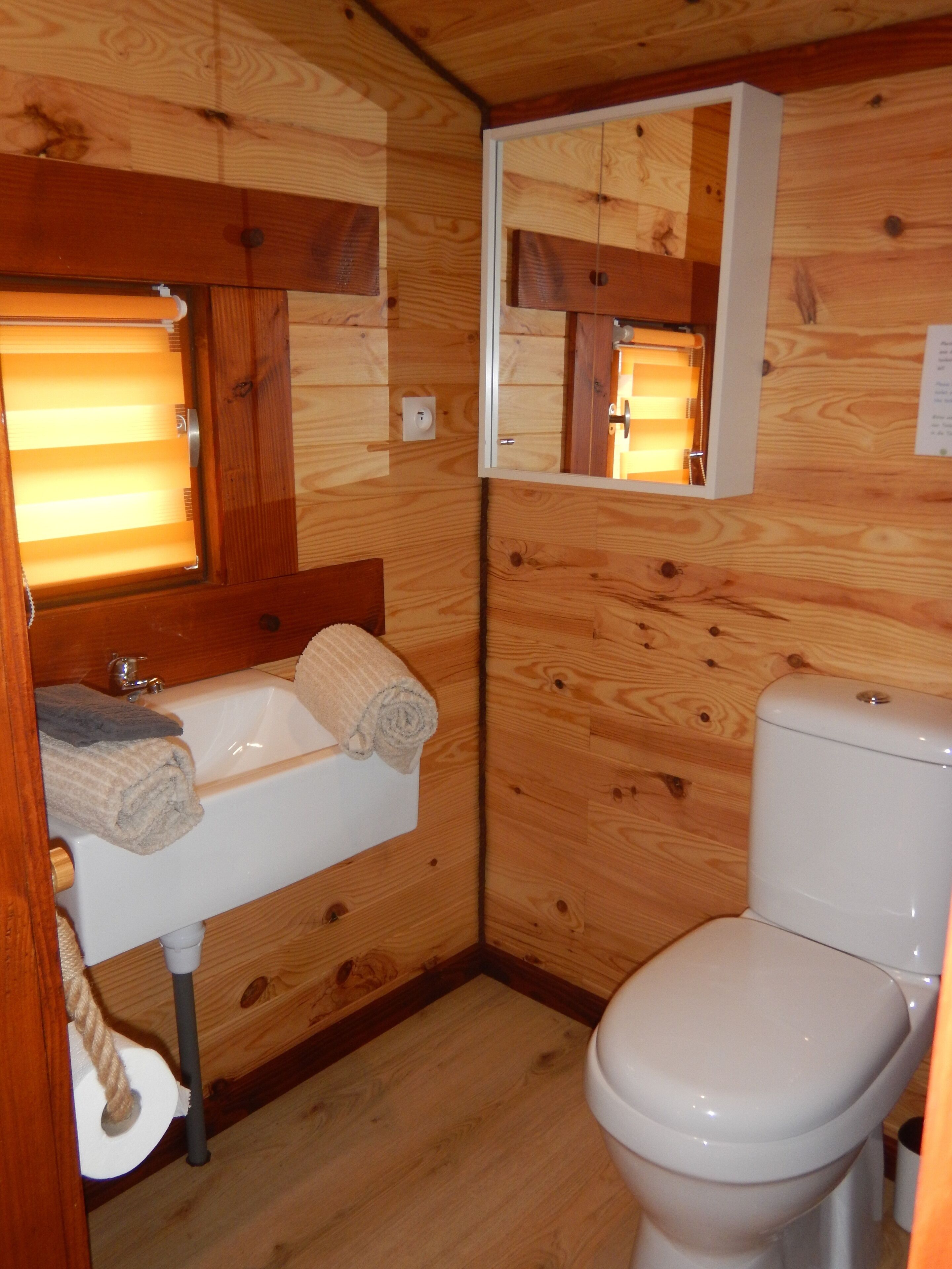 A wooden cabin bathroom with a white sink, a mirror, and a toilet.