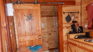 Una cabaña de madera pequeña y acogedora con kitchenette, una mesa y una caja azul, y un espacio para la ducha.