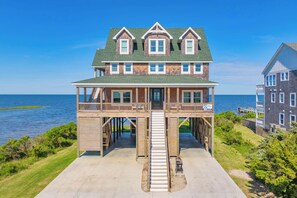 Una casa de dos pisos con un balcón, una escalera que lleva a la terraza y vista al océano.