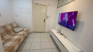A living room with a sofa, a TV mounted on the wall, and a door in the background. - Apto 2 quartos Centro de BC (Balneário Camboriú)