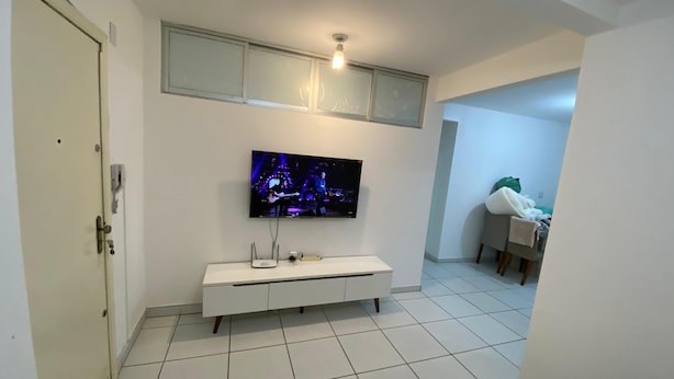 A modern living room with a flat-screen TV mounted on the wall, a white entertainment unit, and a tiled floor. - Apto 2 quartos Centro de BC (Balneário Camboriú)