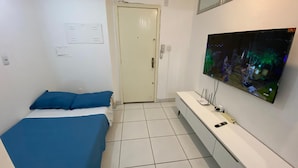 A bedroom with a bed, a TV mounted on the wall, and a small bedside table. - Apto 2 quartos Centro de BC (Balneário Camboriú)