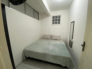 A small, single-bed room with a window, a door, and a ceiling fan. - Apto 2 quartos Centro de BC (Balneário Camboriú)