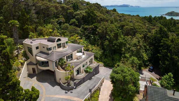 Una casa moderna con techo curvo, rodeada de abundante vegetación y vista al mar.