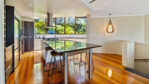 Una cocina moderna con una isla de vidrio, electrodomésticos de acero inoxidable y un amplio ventanal con vistas a un jardín exuberante.
