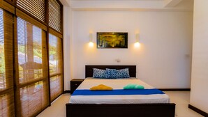 A bedroom with a bed, a nightstand, a wall-mounted painting, and a sliding door with a view. - White House 101 (Galle)