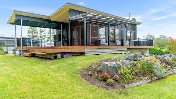 A modern house with a covered patio, a deck, and a landscaped garden. - Summer Haze - Omaha Holiday Home (Matakana)