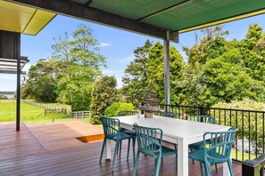 Een overdekt terras met een witte tafel en teal-kleurige stoelen, omgeven door een houten terras en een metalen balustrade.
