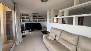 Een woonkamer met een beige bank, een zwarte bank en een boekenplank vol boeken.