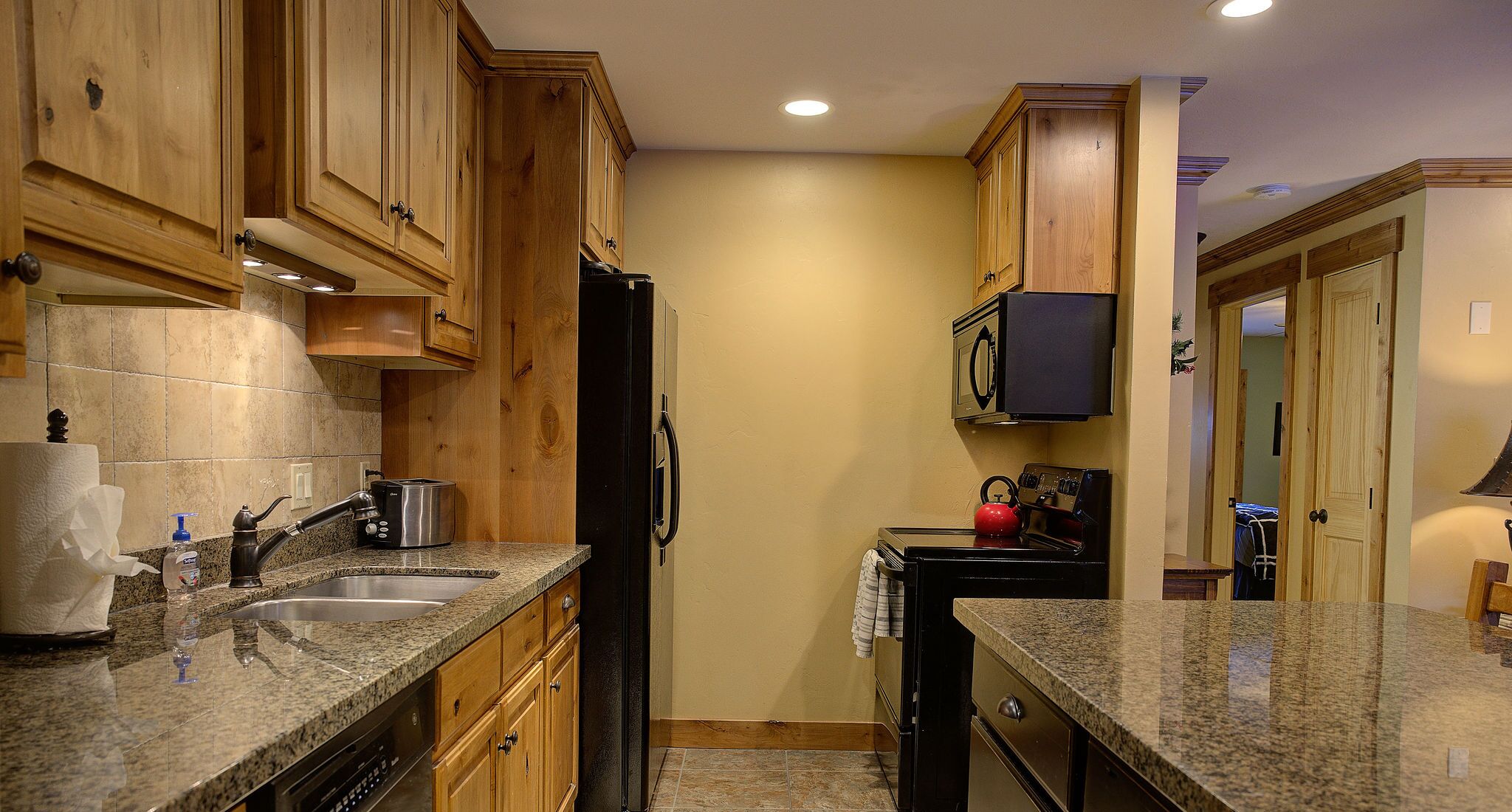 A compact kitchen with wooden cabinets, granite countertops, a stainless steel refrigerator, and a microwave.