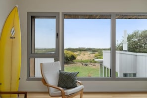 A room with a large window, a chair, and a yellow surfboard.