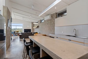 A modern kitchen with a long countertop, bar stools, and a built-in oven.