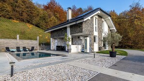 Una casa moderna con fachada de piedra, piscina y un patio con sillones de descanso.