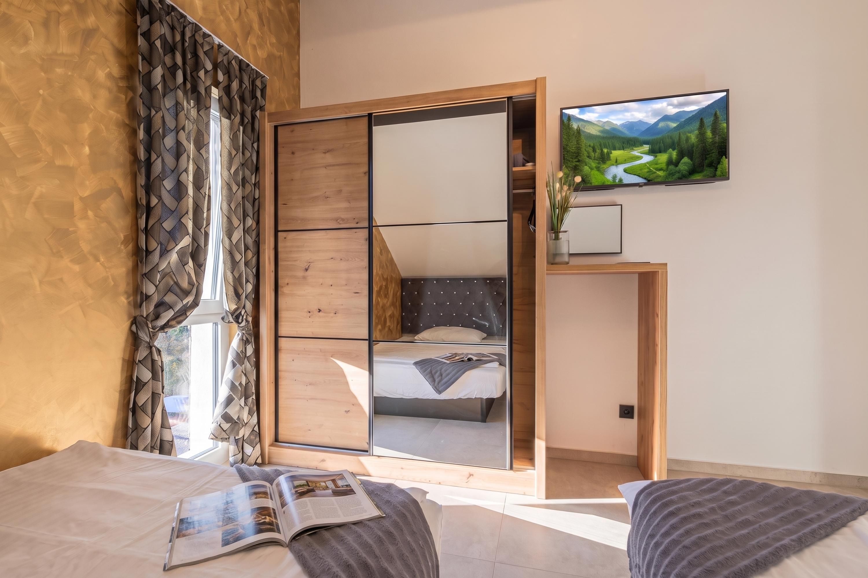 A modern bedroom with a large bed, a bedside table, a mirror, and a TV mounted on the wall.